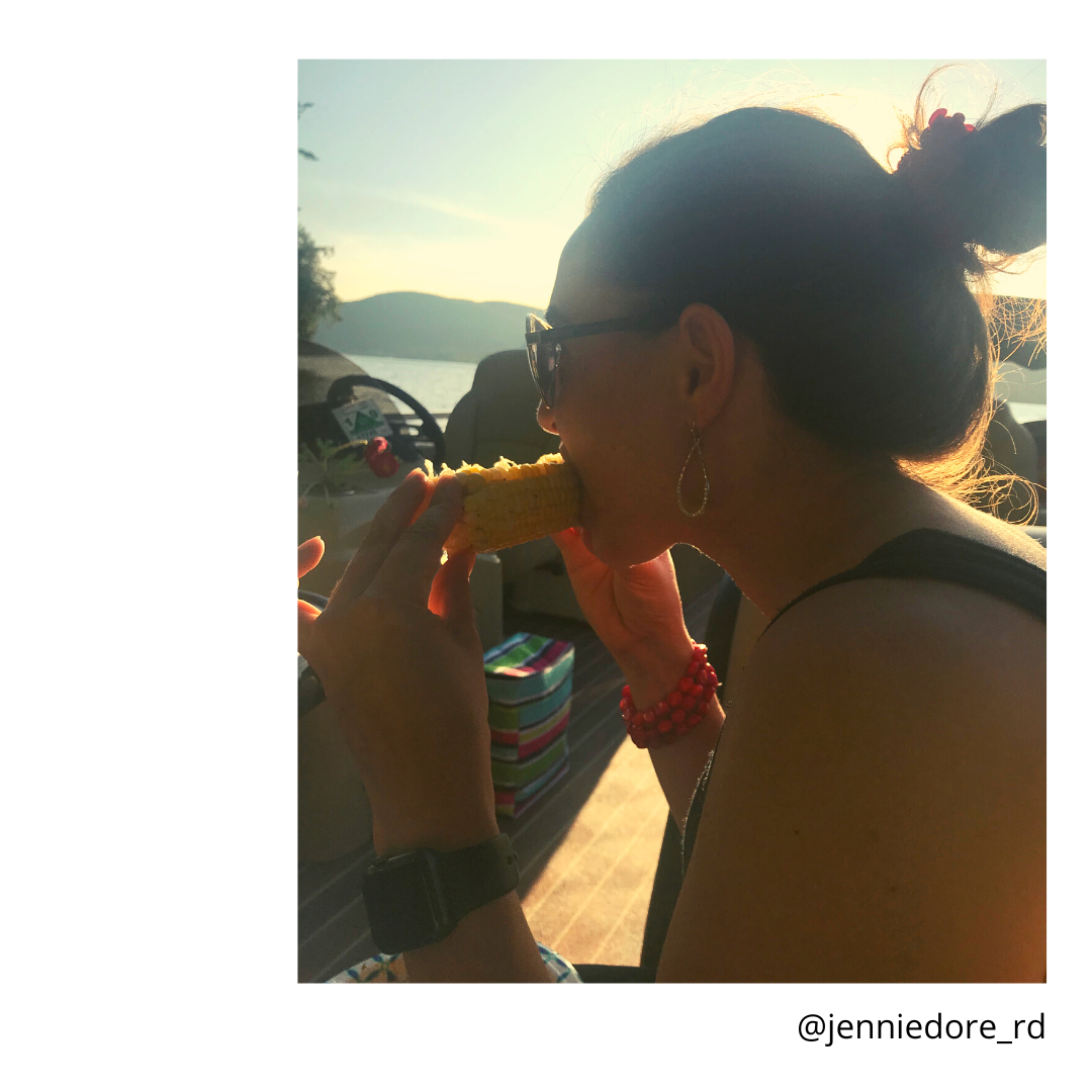 girl with brown hair in a bun eating corn in the sun.