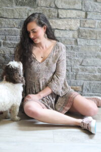 white small dog looking at girl in a dress sitting on the floor 