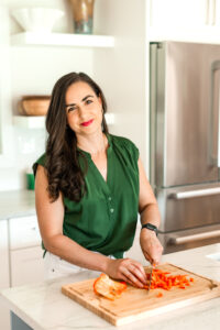 brown hair girl smiling while cutting a bell pepper in the kitchen